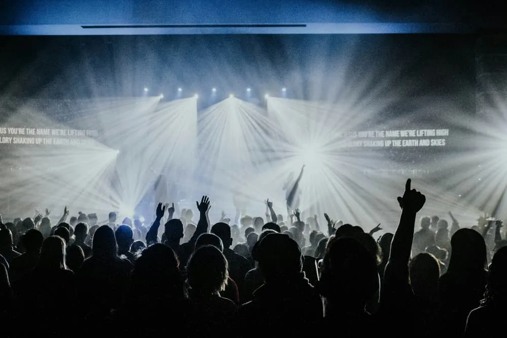 Congregation facing a worship stage with white beams through haze