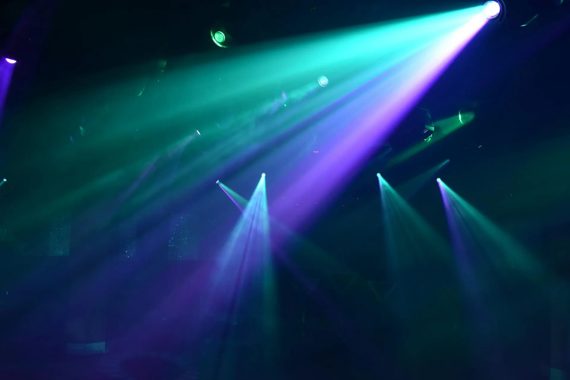 Moving-head light beams in teal and purple cutting through haze